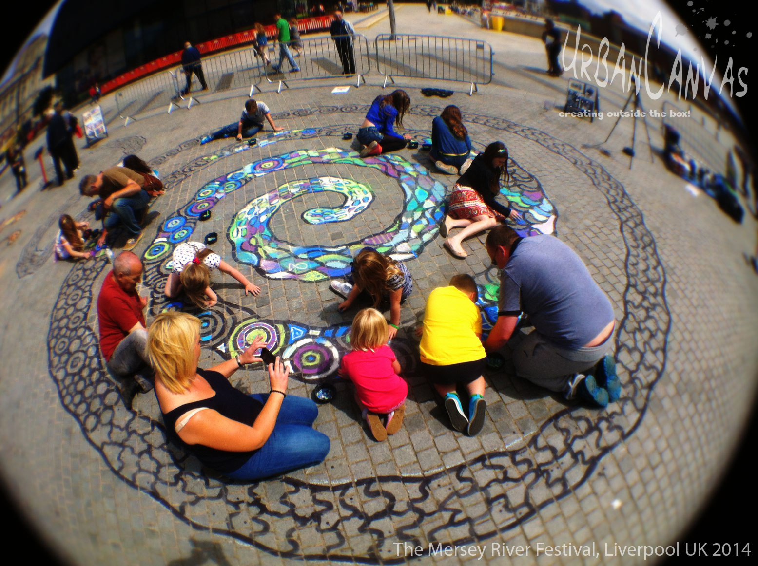 Photograph of the work of urban canvas - several families crouching over a chalk, spiral river.