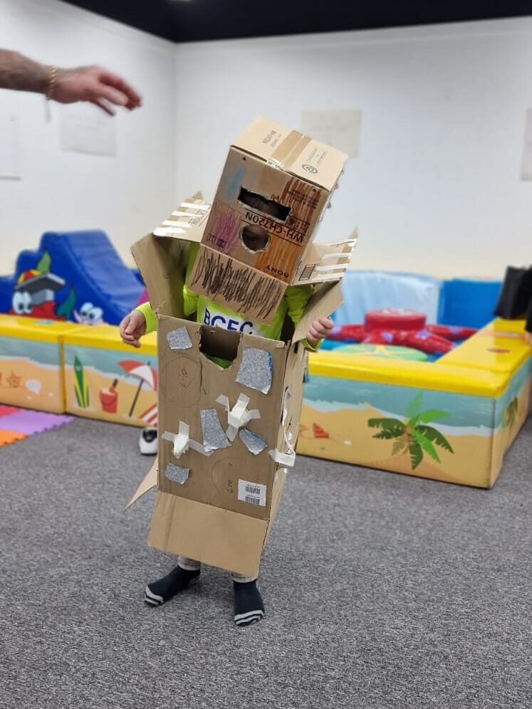 A child dressed in a cardboard robot suit, decorated and made of boxes - they pose!