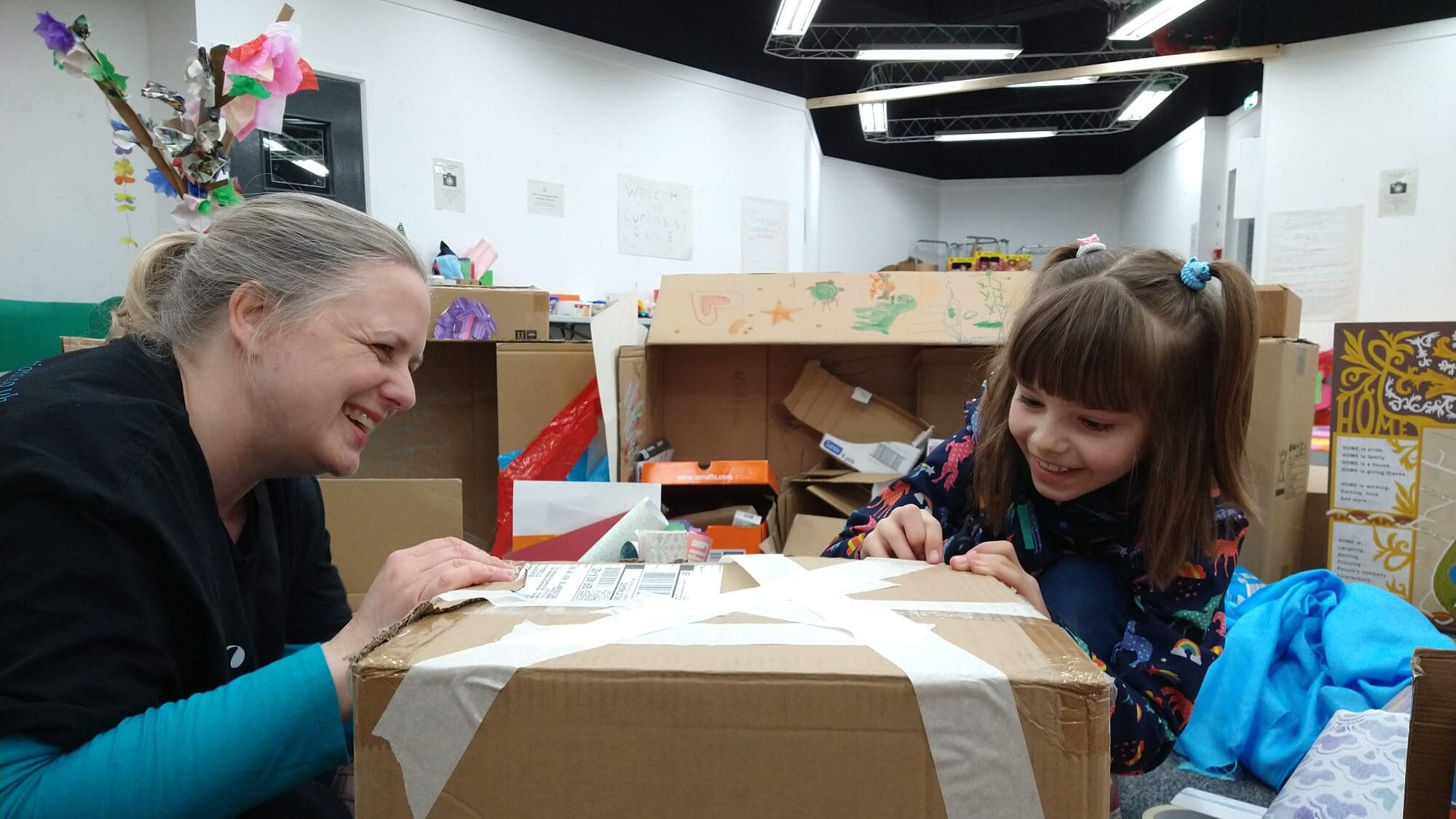 Photo of child and facilitator, taping a cardboard box down and smiling.