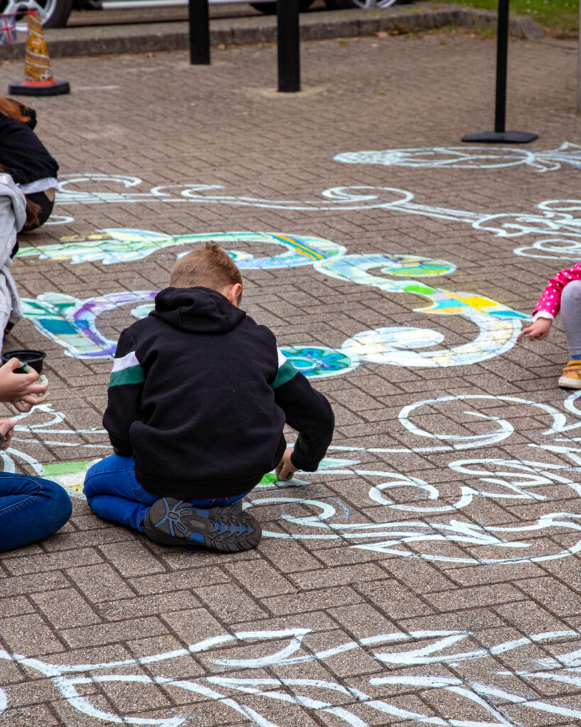 An image of children doing chalk art on the floor, outdoors.