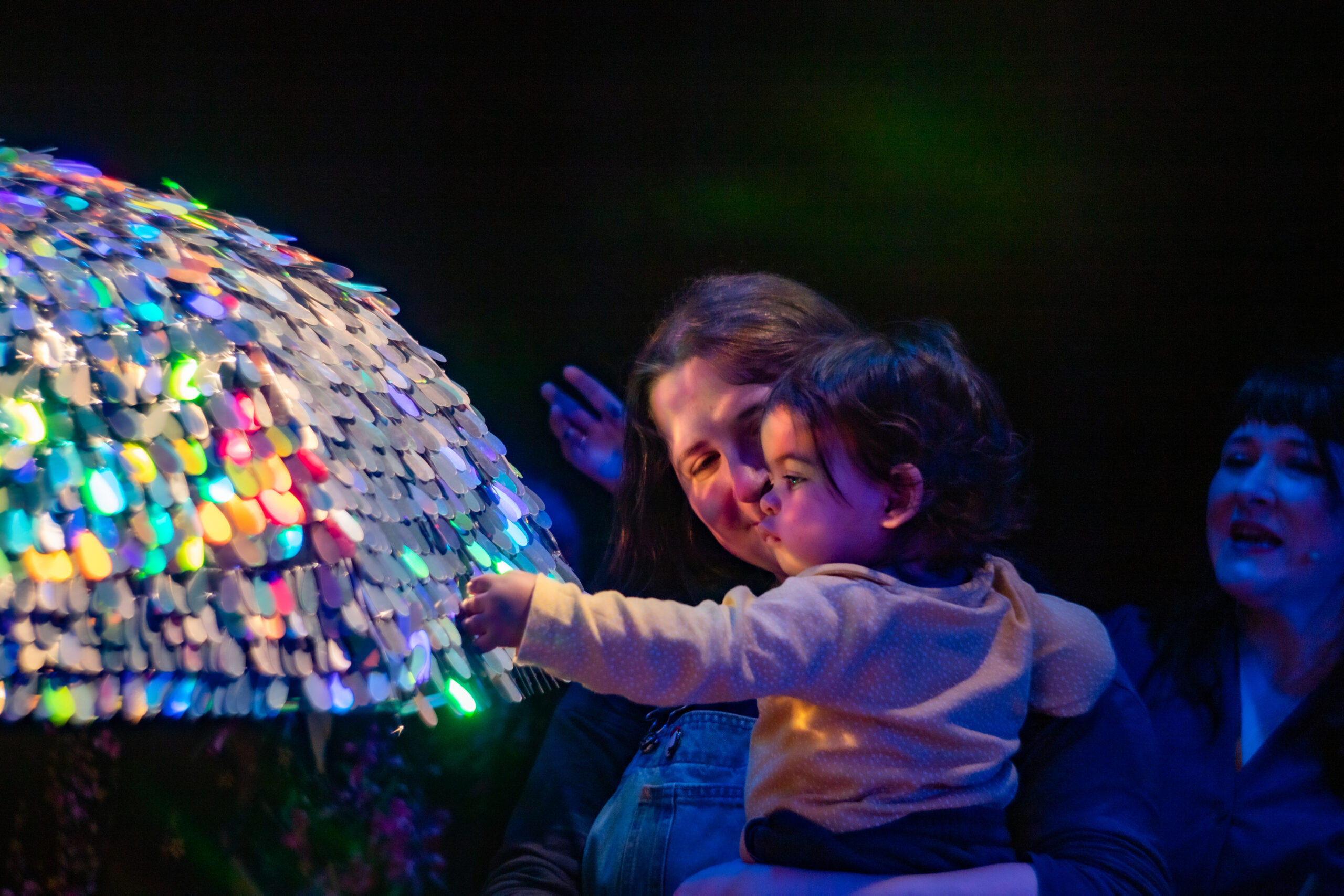 A mother holding her baby, the baby is staring at a decorated and lit colourful umbrella