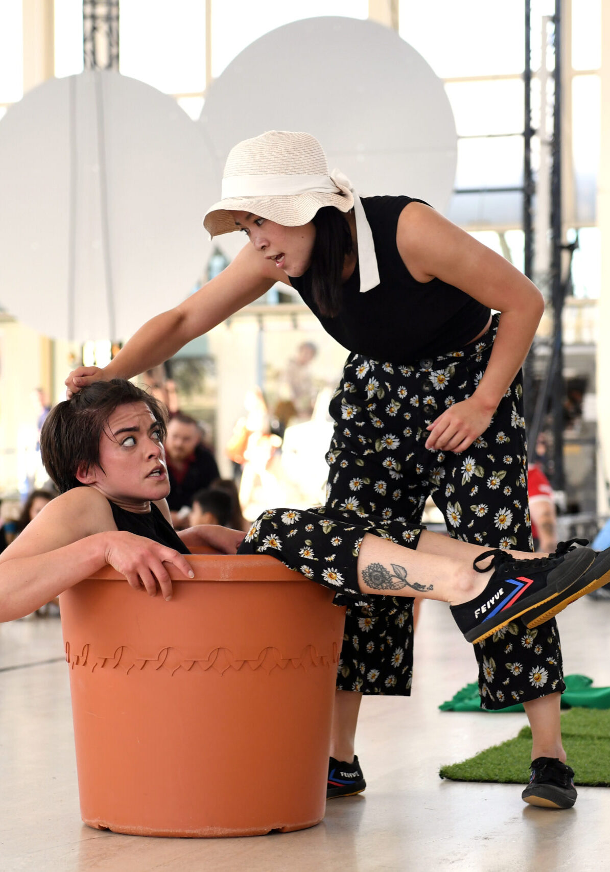 A photo of two dancers, one fallen into a large flower pot and the other leaning over them.